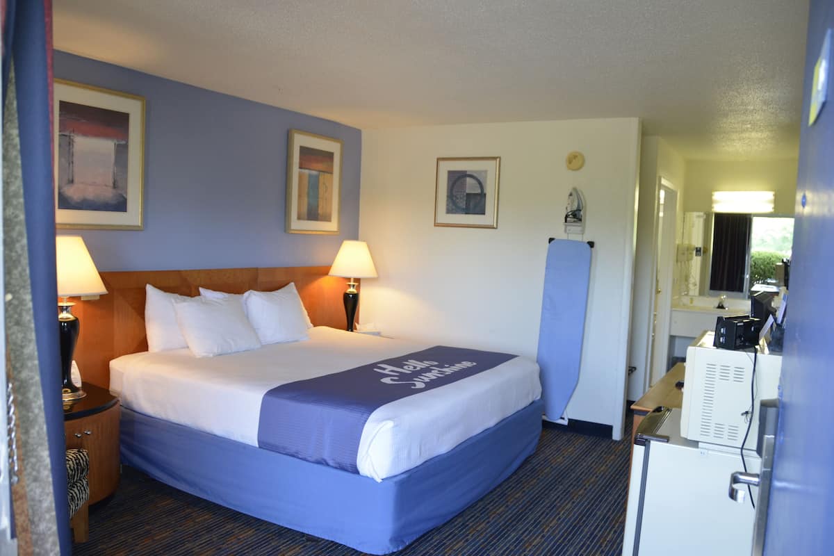 A hotel room with a bed, two bedside lamps, a nightstand, a dresser, and a mirror.