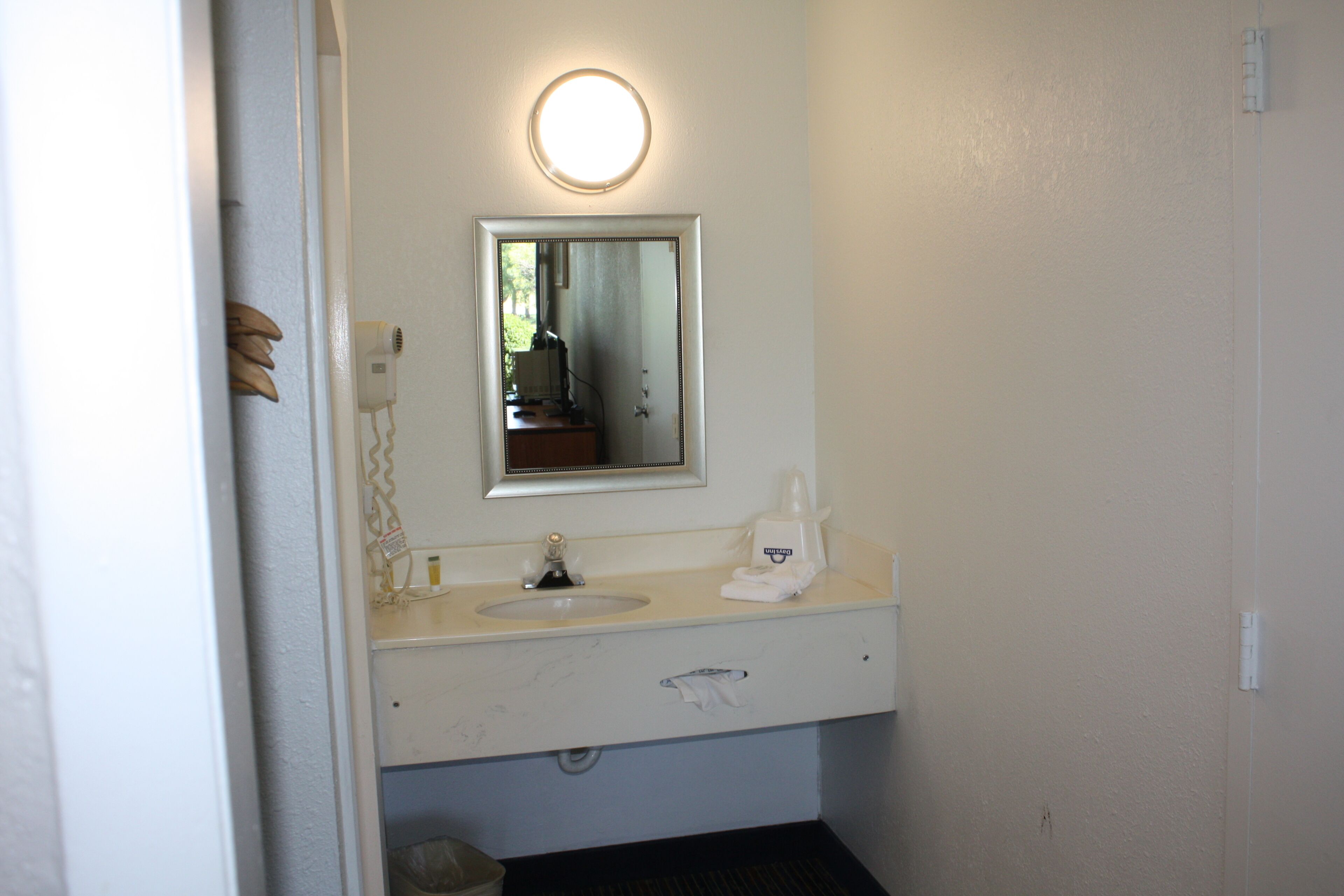 A bathroom with a white sink, a mirror with a round light, and a towel dispenser.
