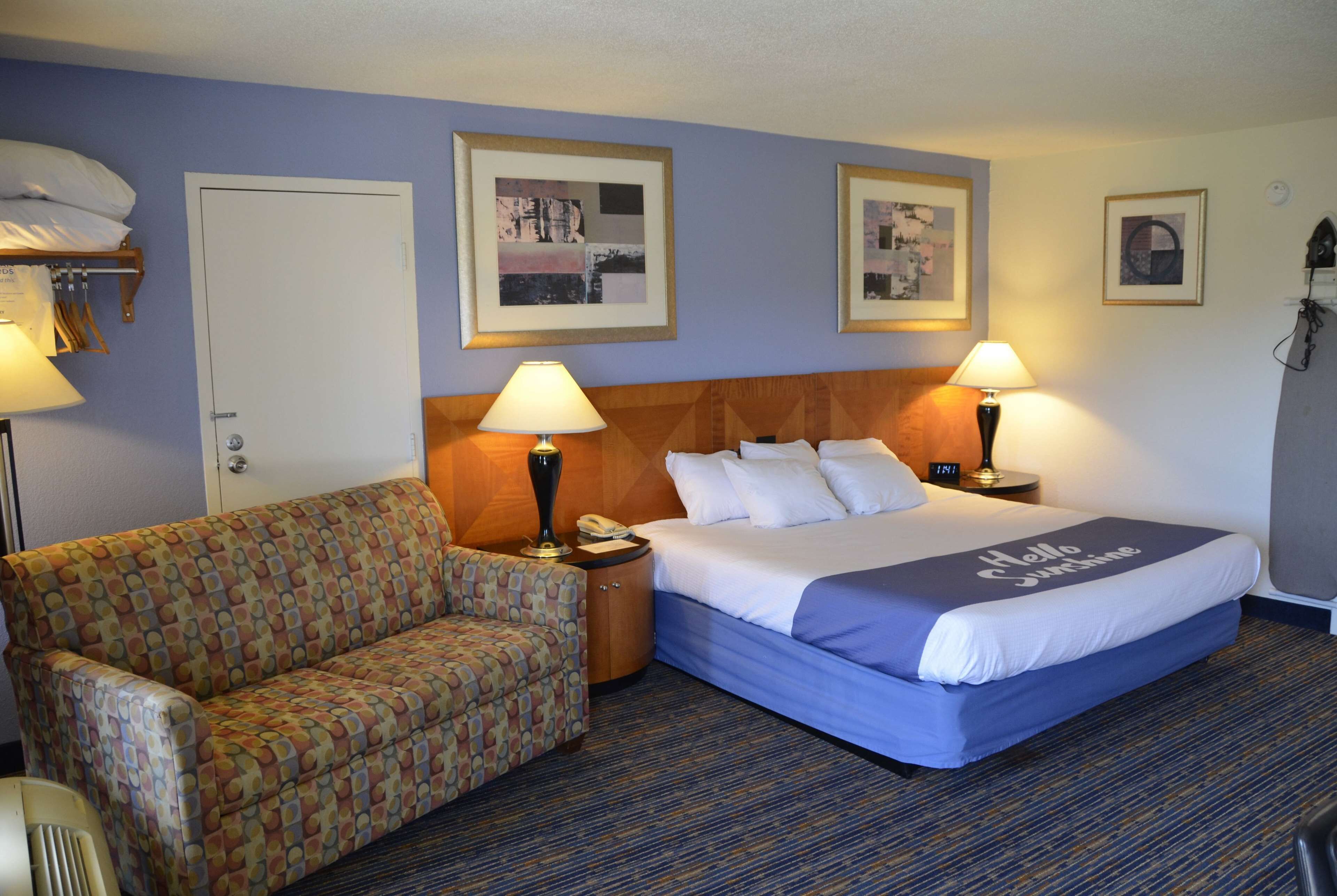 A hotel room with a bed, a sofa, two lamps, and framed pictures on the wall.