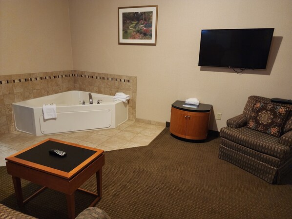 A room with a bathtub, a television, a sofa, and a small table with a remote control. - Days Inn by Wyndham Luray Shenandoah (Luray)