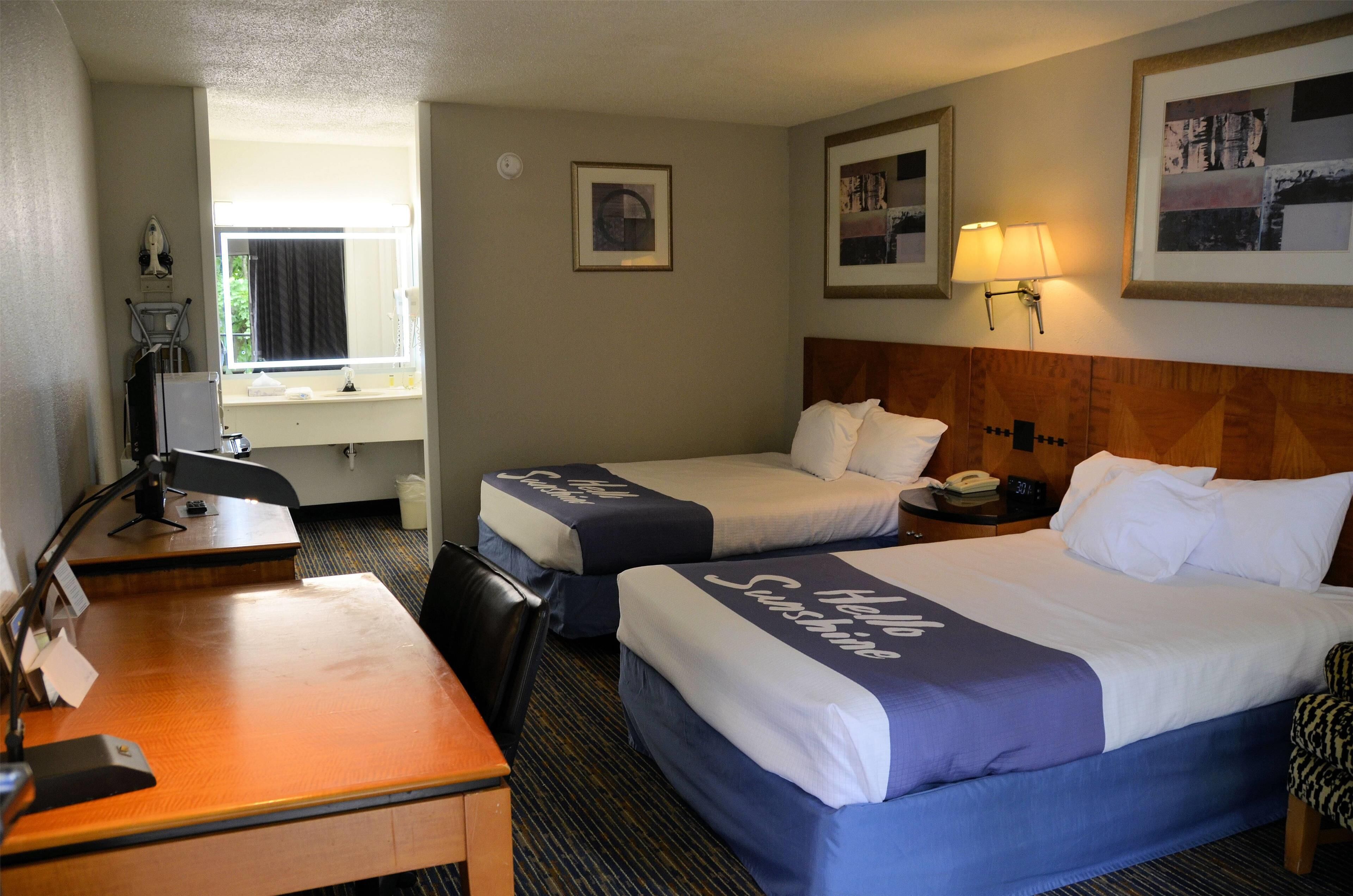 Une chambre d’hôtel avec deux lits, un bureau, une chaise, une lampe et une fenêtre.