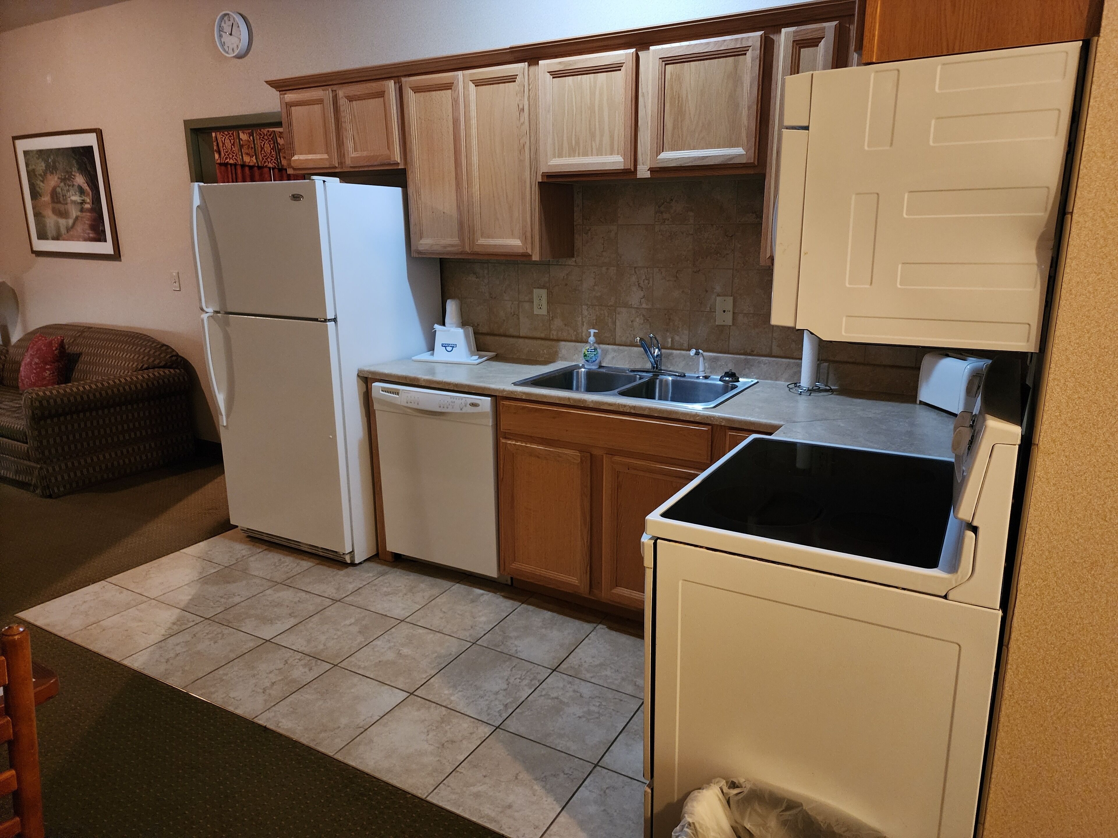 A compact kitchen with wooden cabinets, a white refrigerator, a dishwasher, and a black stove.