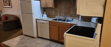 A compact kitchen with wooden cabinets, a white refrigerator, a dishwasher, and a black stove.