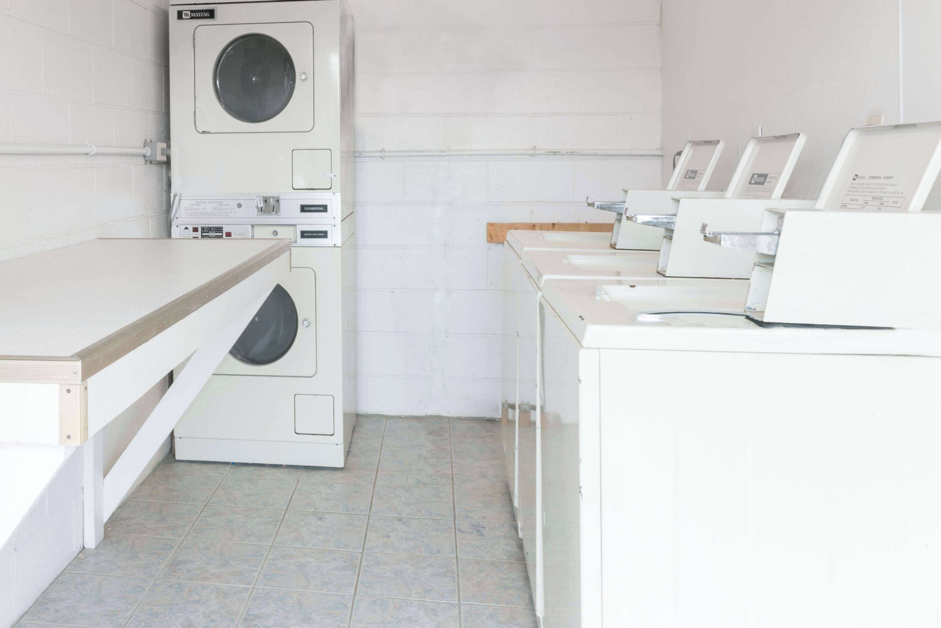 A laundry room with a stacked washer and dryer, a drying rack, and multiple washing machines.