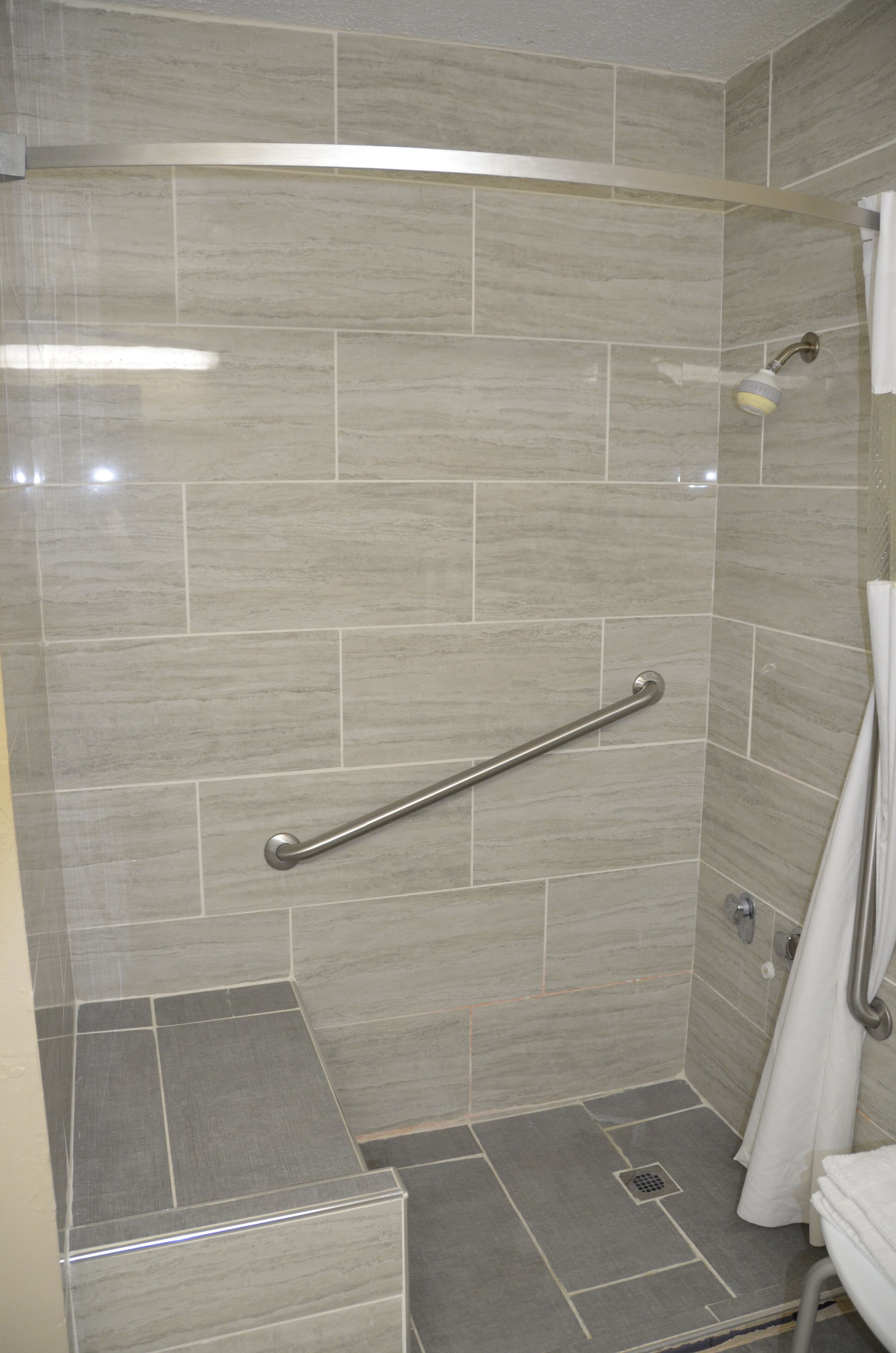 A shower with a grab bar, tiled walls, and a shower curtain.