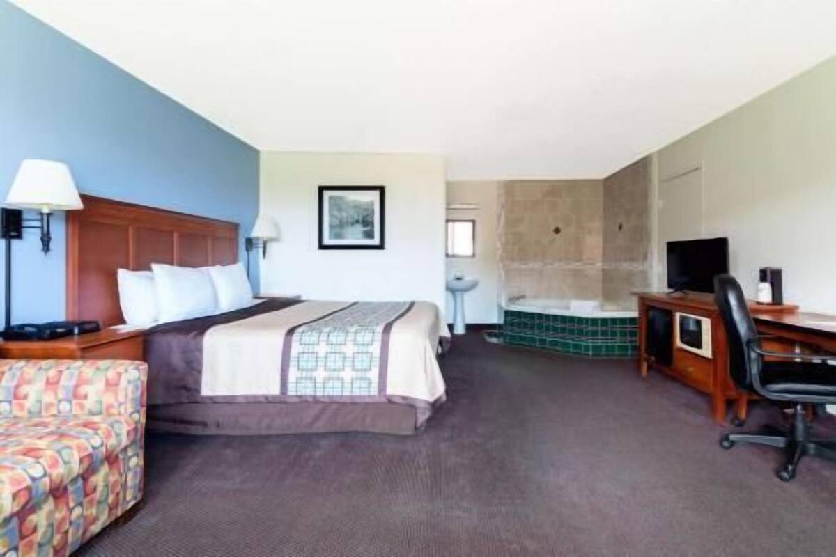 A hotel room with a bed, desk, chair, and a shower area.