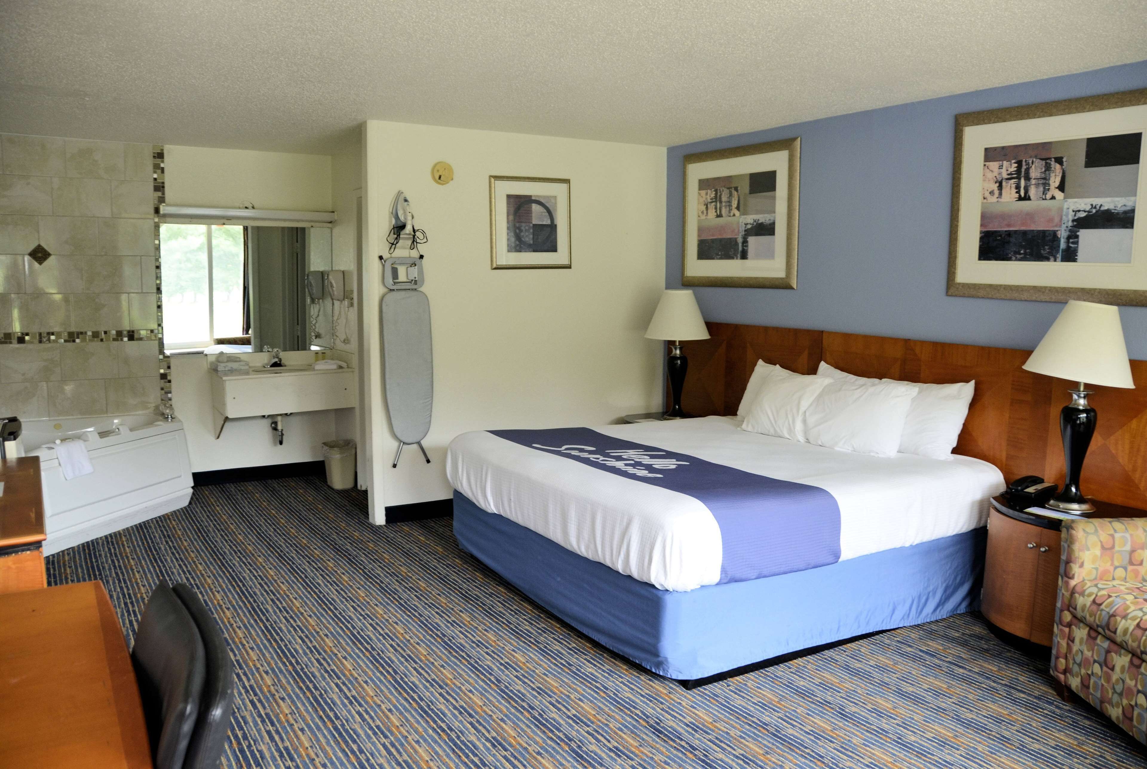 A hotel room with a bed, a desk, a chair, a mirror, a vanity, and a window.