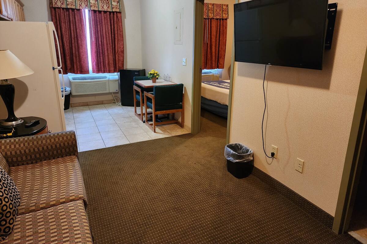 A hotel room with a bed, a desk with a chair, a television, a lamp, and a waste bin.