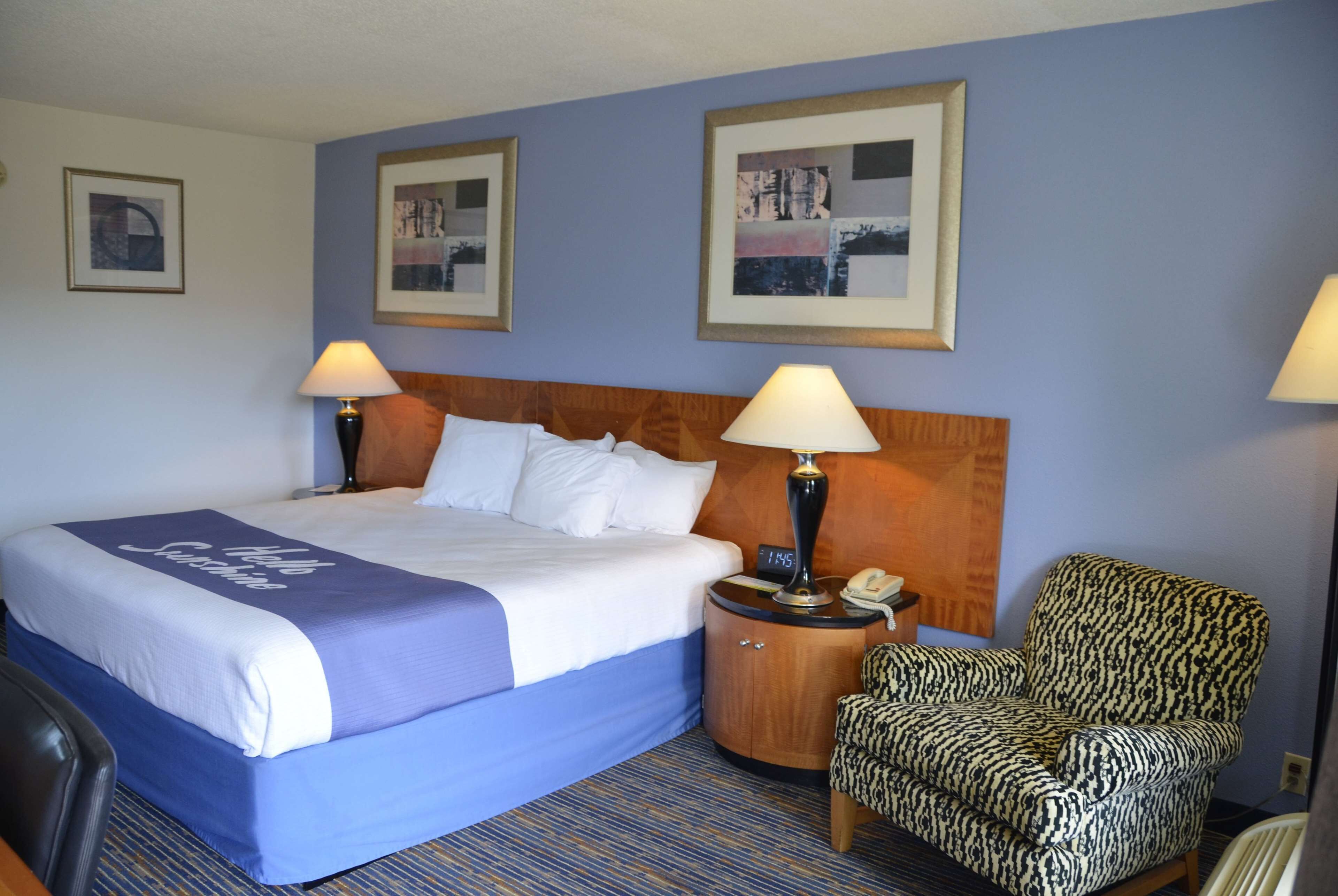 A hotel room with a large bed, two bedside lamps, a chair, and framed pictures on the wall.