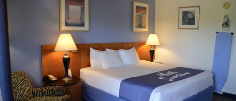 Ein Hotelzimmer mit einem großen Bett, zwei Nachttischlampen, einem Sessel und Bildern an den Wänden.