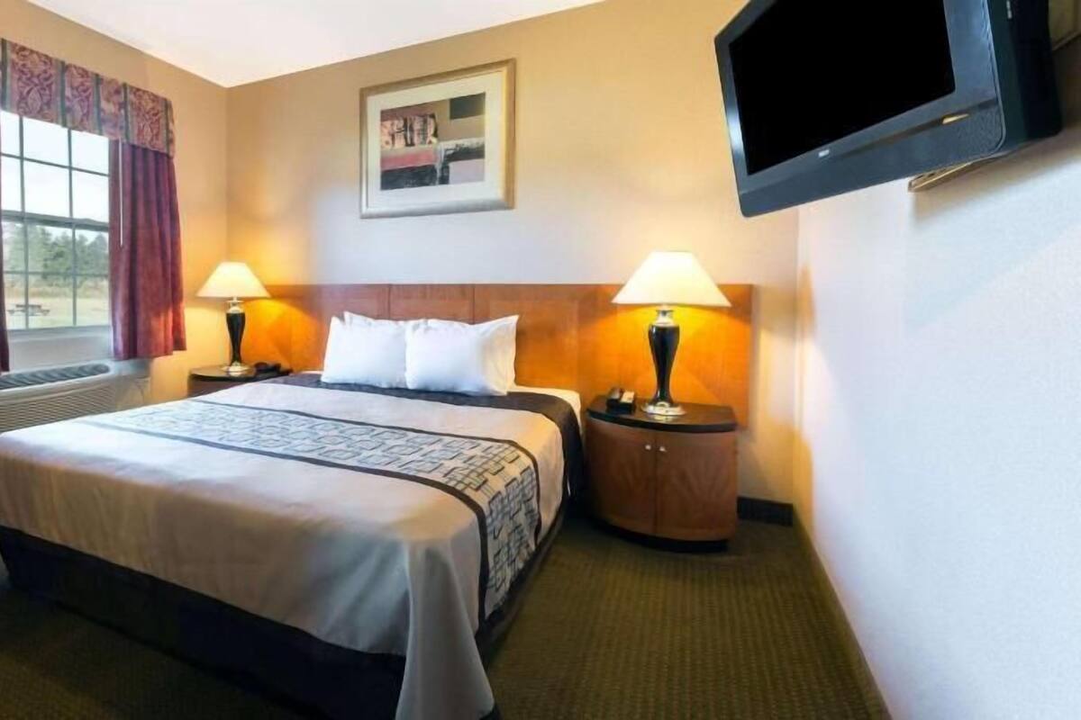 A hotel room with a bed, two bedside tables with lamps, a TV mounted on the wall, and a window with curtains.