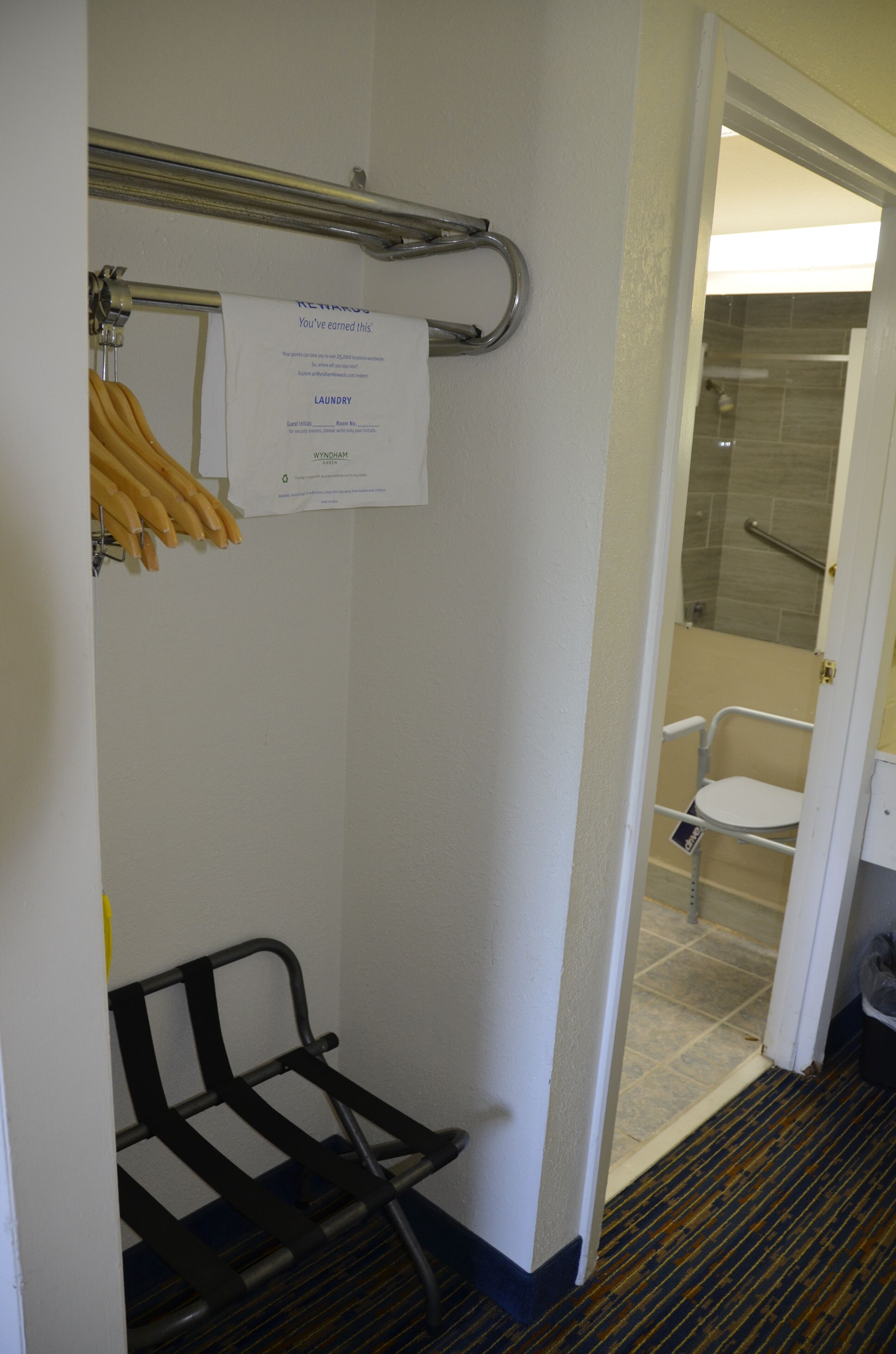 A hotel bathroom with a shower, a toilet, and a bench. There is a sign on the wall and a towel rack with towels.