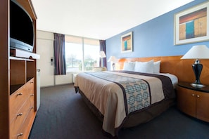 A hotel room with a large bed, a dresser, a television, and a window with curtains.