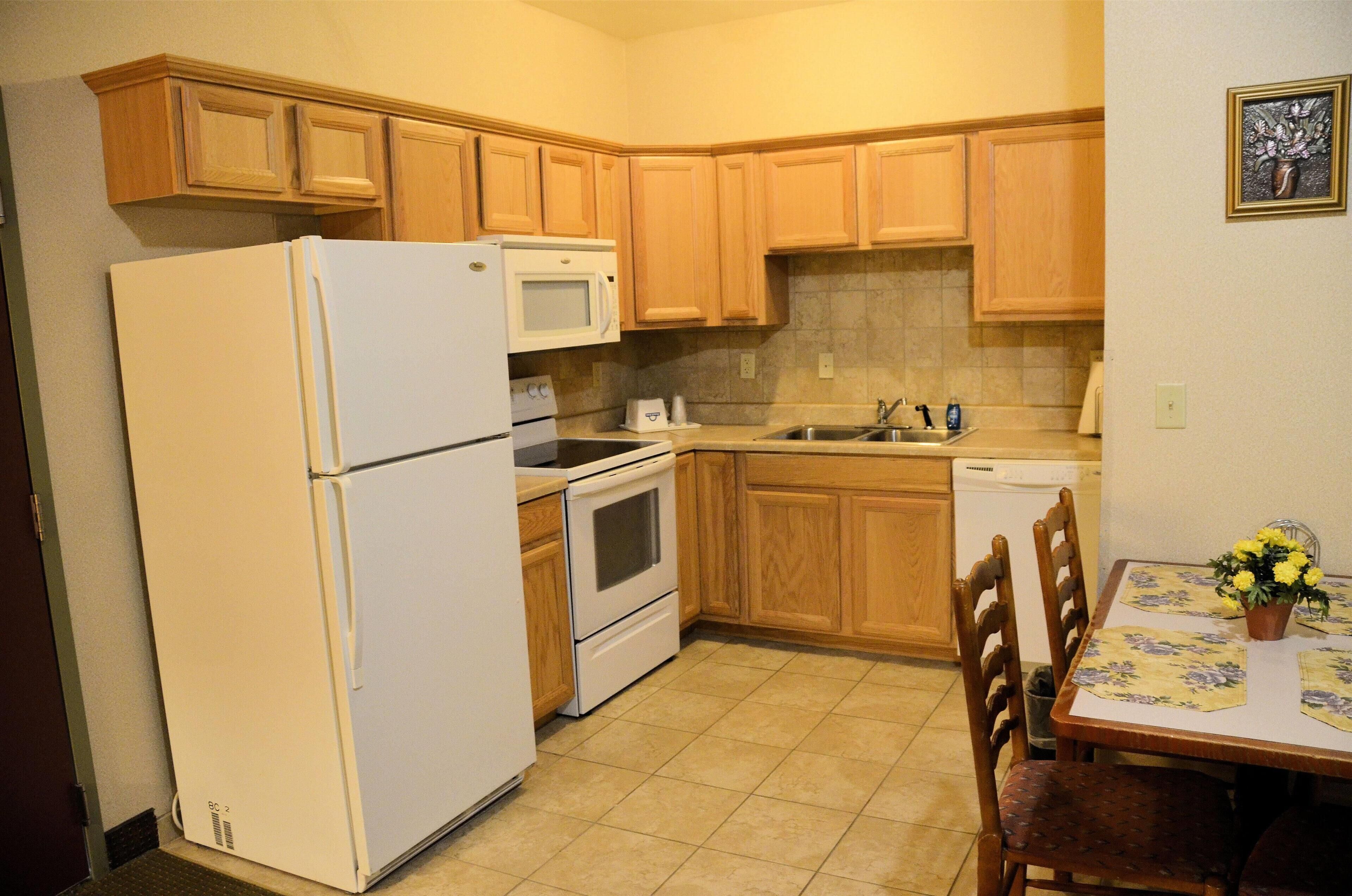 A compact kitchen with wooden cabinets, a refrigerator, microwave, oven, and a dishwasher.