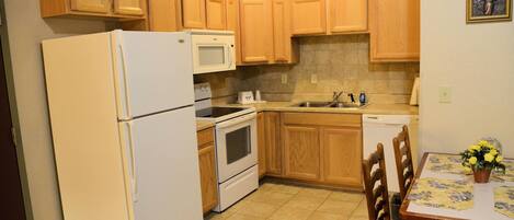 A compact kitchen with wooden cabinets, a refrigerator, microwave, oven, and a dishwasher.