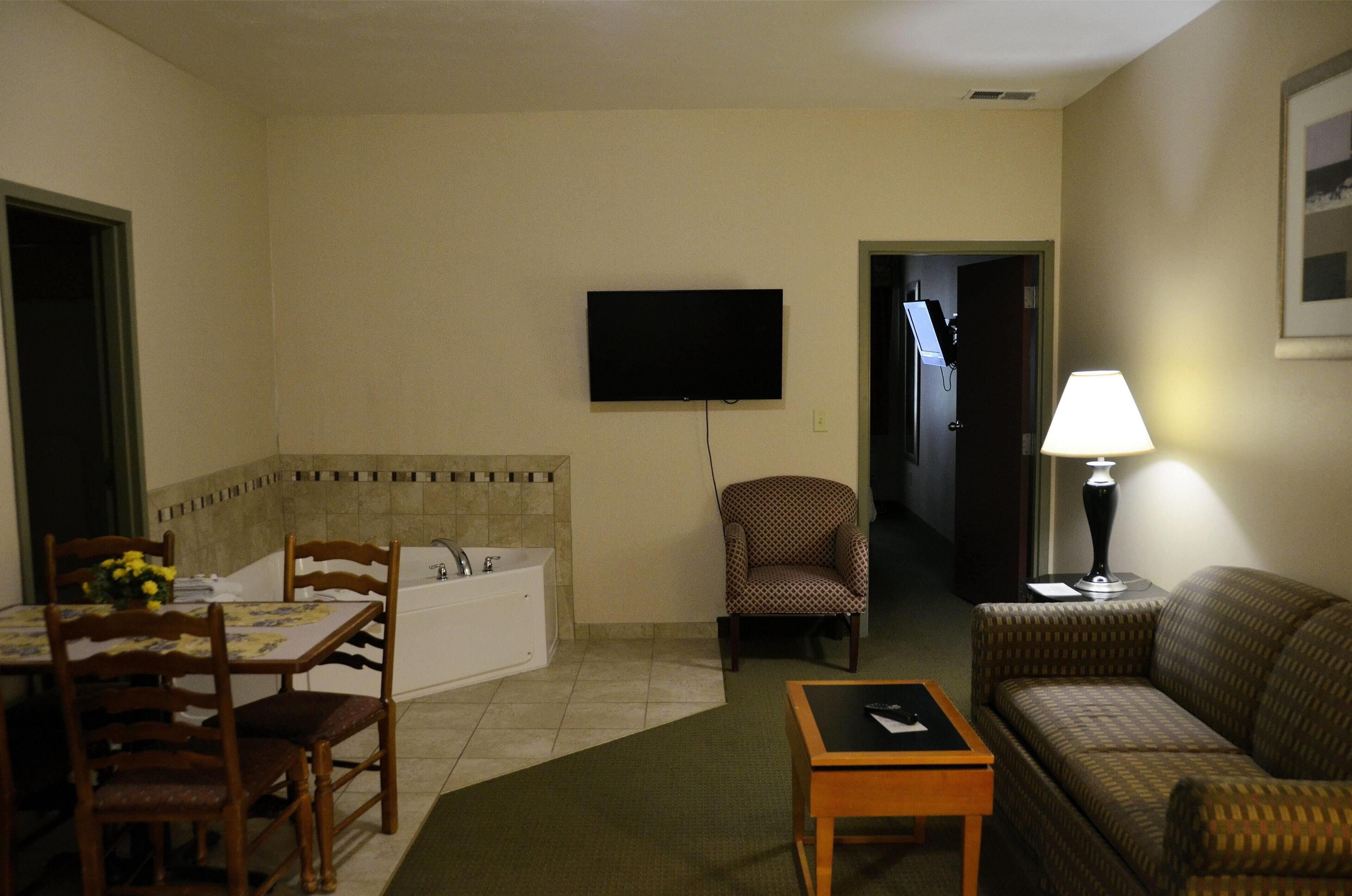 A living room with a sofa, a table, a chair, a television, a lamp, and a bathroom with a bathtub.