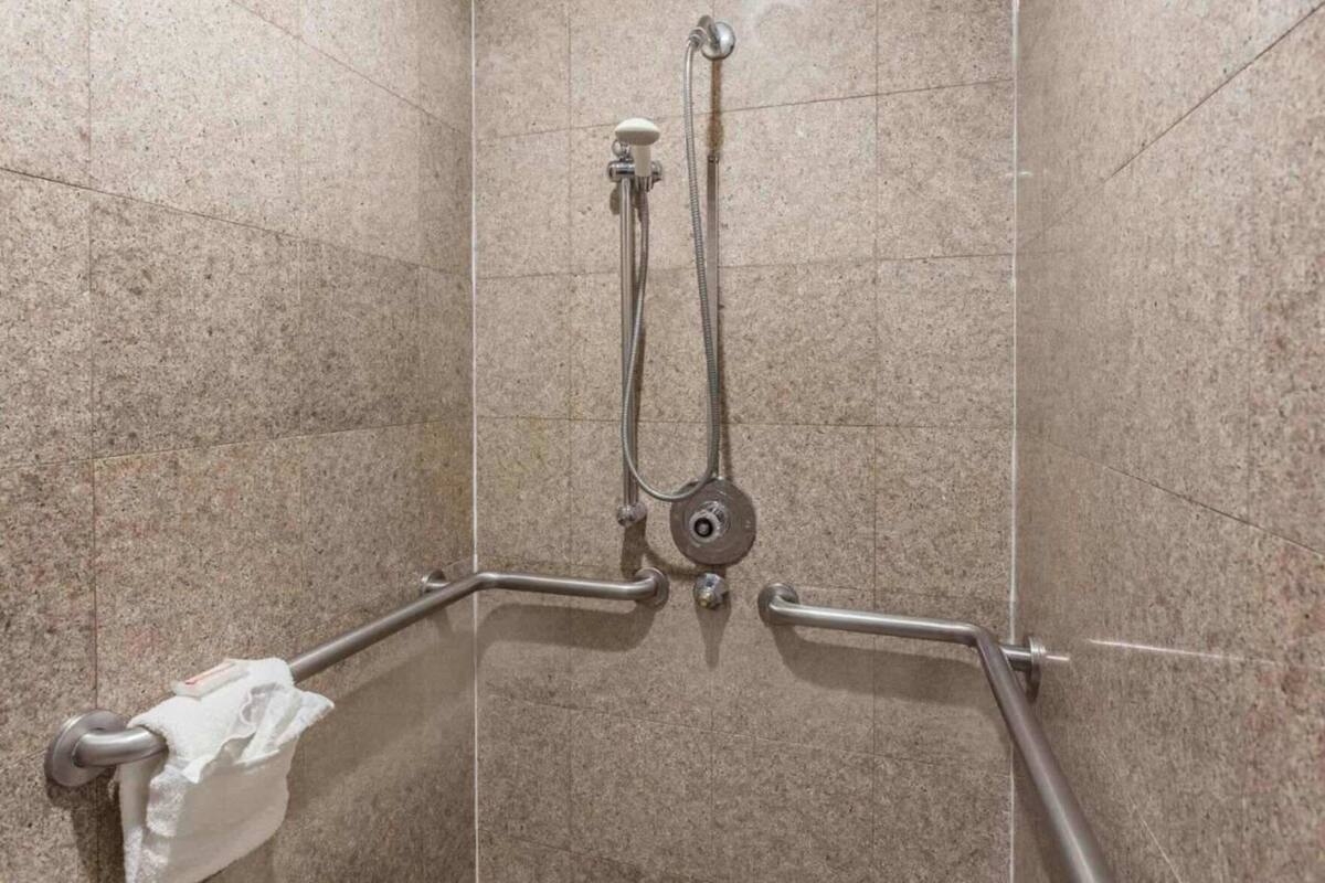A shower area with a handheld showerhead, a wall-mounted faucet, and a grab bar for support.