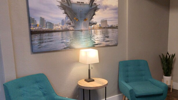 A room with two teal armchairs, a small round table with a lamp, and a large cityscape painting on the wall. - SureStay Hotel by Best Western Chula Vista San Diego Bay (Chula Vista)
