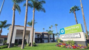 A SureStay Hotel sign with a clear view of the building, palm trees, and a well-maintained lawn. - SureStay Hotel by Best Western Chula Vista San Diego Bay (Chula Vista)
