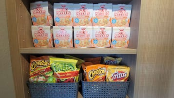 A shelf stocked with Nissin Cup Noodles in chicken flavor and various brands of Tostitos chips.