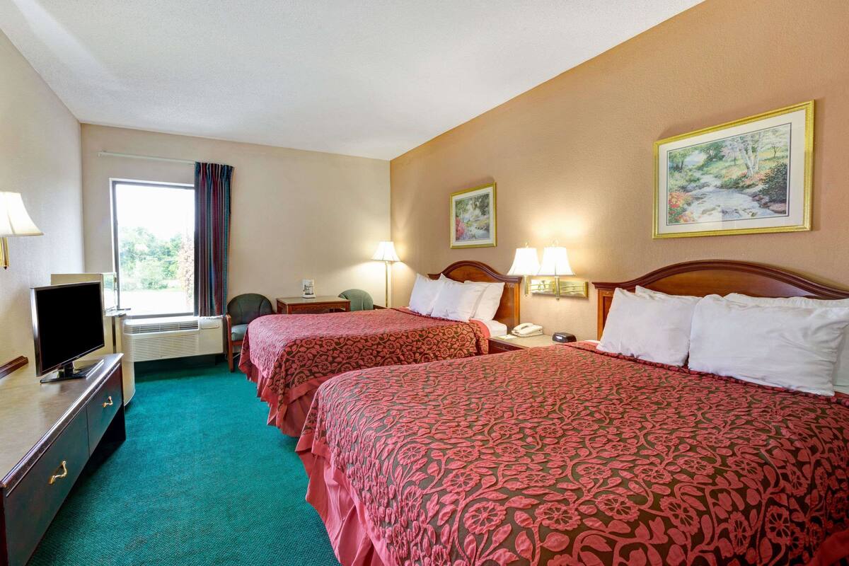 A hotel room with two beds, a television, a desk, and a window with curtains.