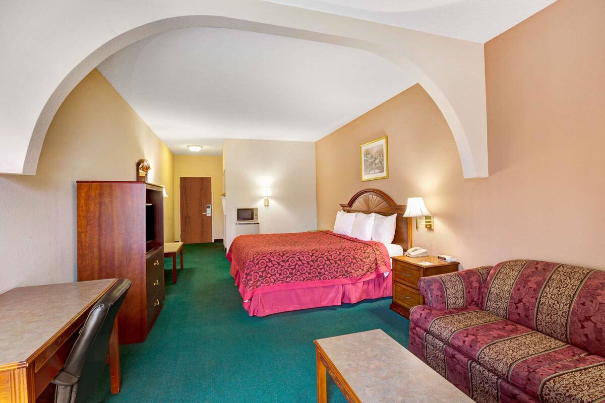 A hotel room with a bed, a desk, a chair, a sofa, and a dresser.