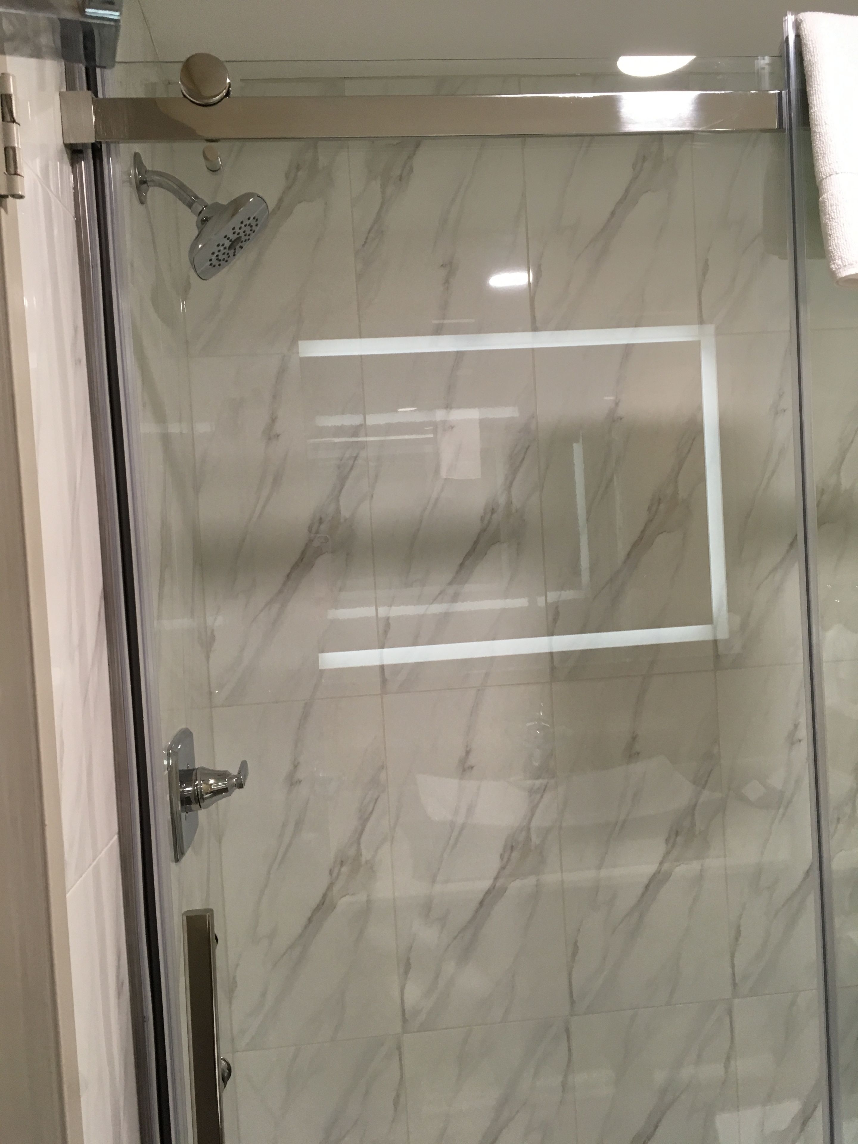 Eine begehbare Dusche mit Glastrennwand, einer Handbrause und einer wandmontierten Armatur.
