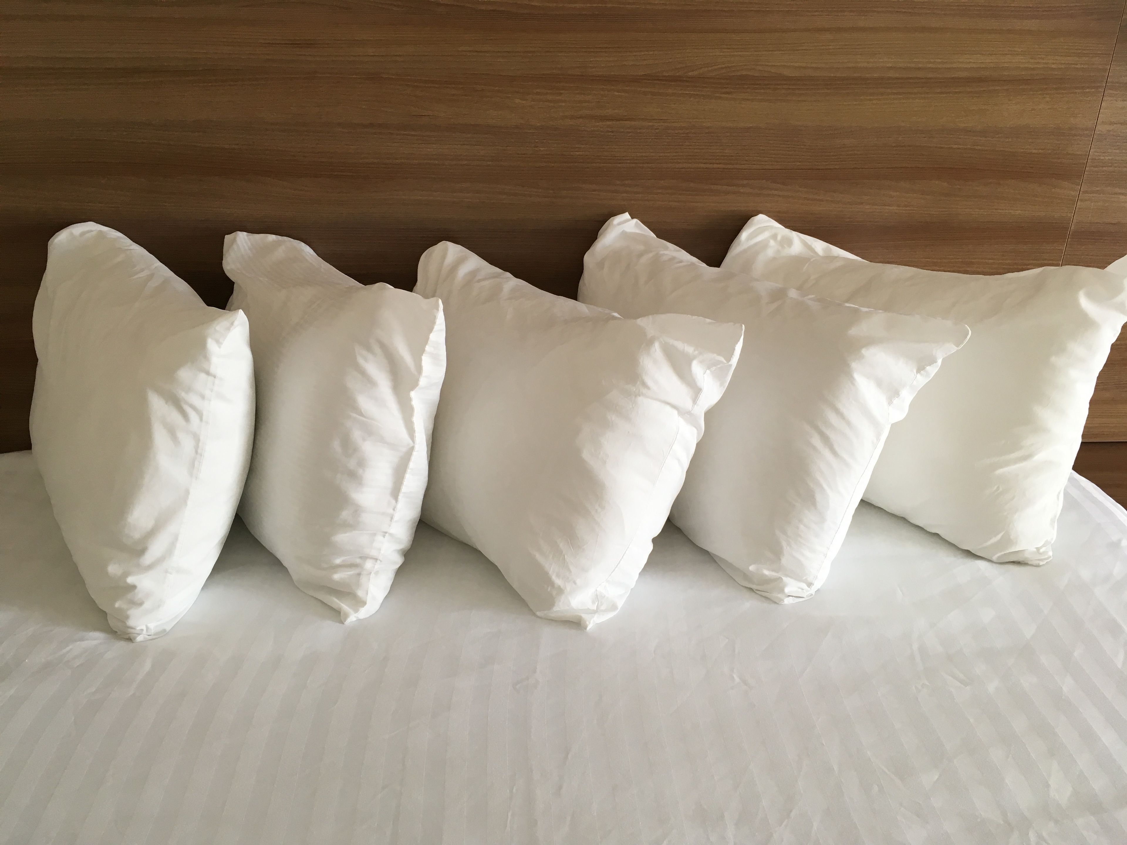 A bed with five white pillows against a wooden headboard.