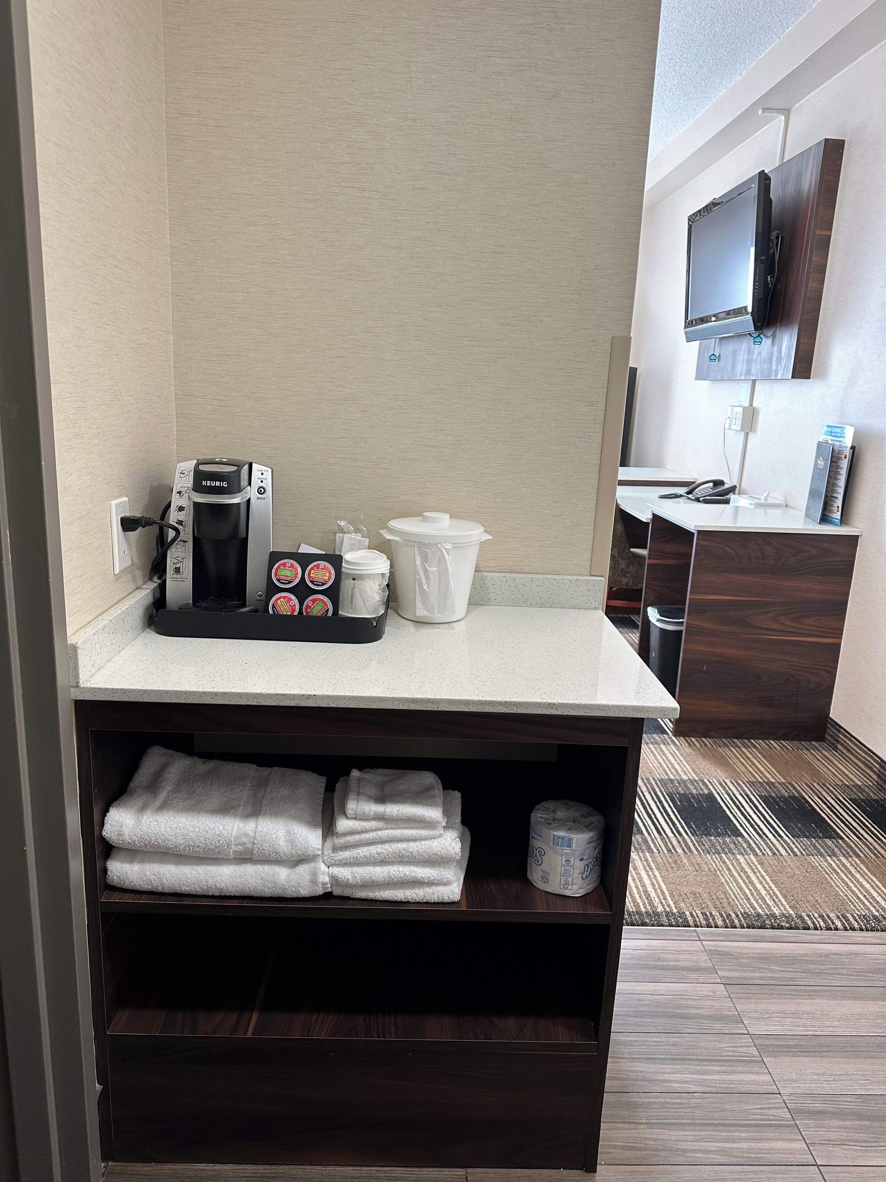 Une salle de bain d’hôtel équipée d’une machine à café, de produits de toilette et d’un téléviseur fixé au mur.