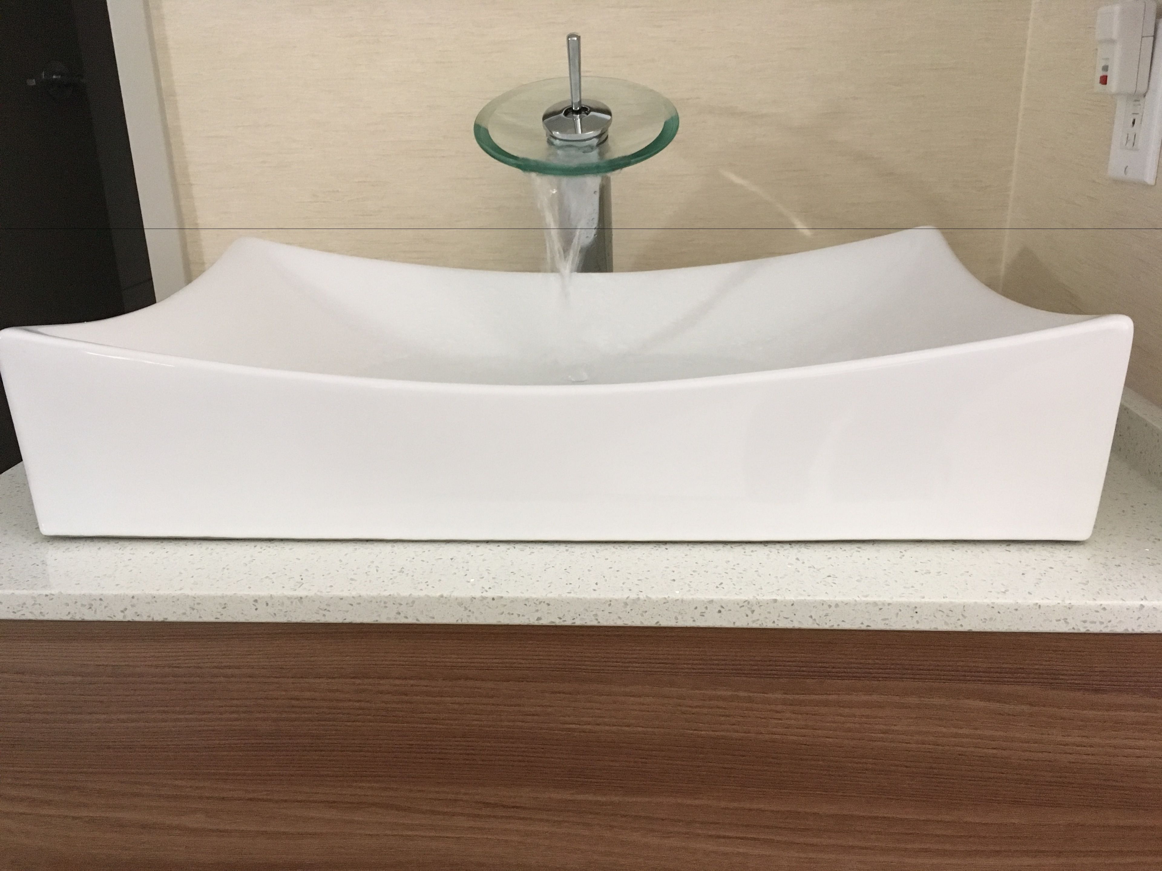 A white, modern bathroom sink with a glass pedestal faucet.