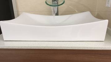 A white, modern bathroom sink with a glass pedestal faucet.