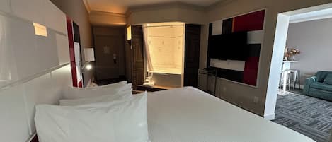 Habitación de hotel con una cama grande, un escritorio, una silla, un televisor y una mesita con un florero.