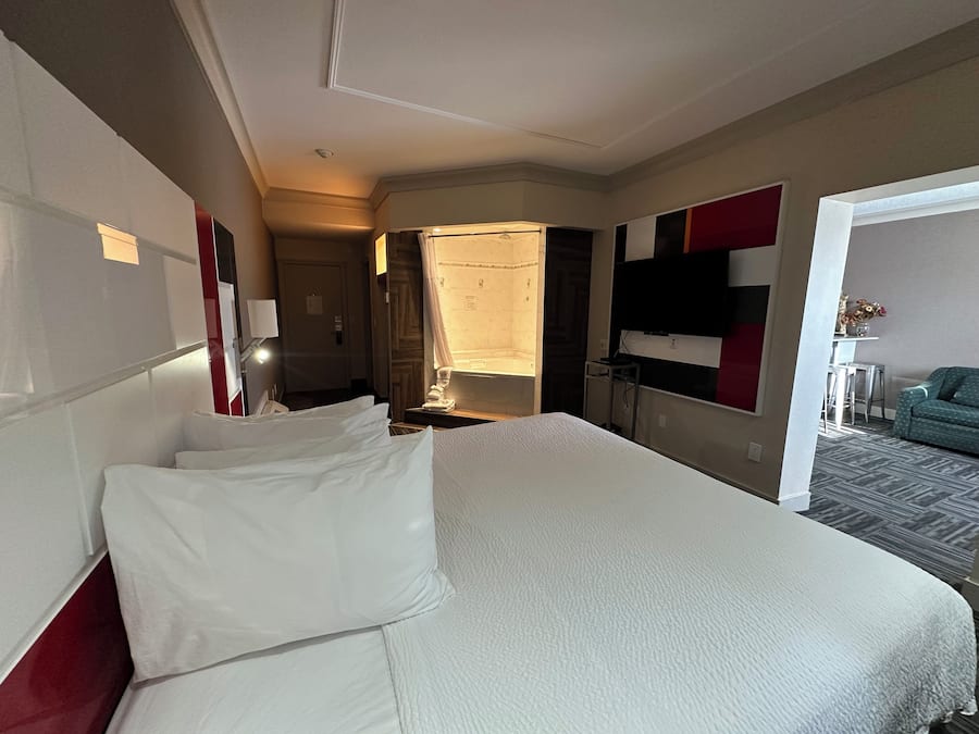 Une chambre d’hôtel avec un grand lit, un bureau, une chaise, une télévision et une petite table sur laquelle se trouve un vase.