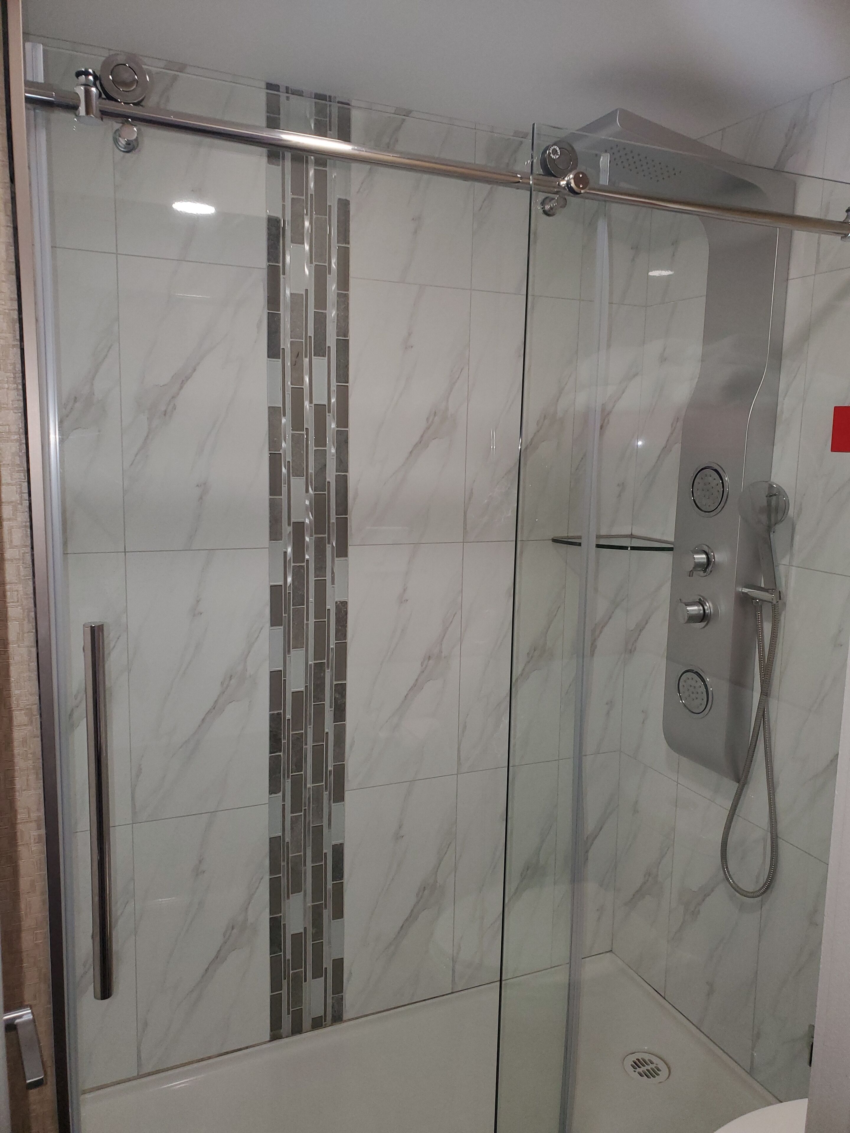 A glass-enclosed shower with a tiled wall and a metal handle.