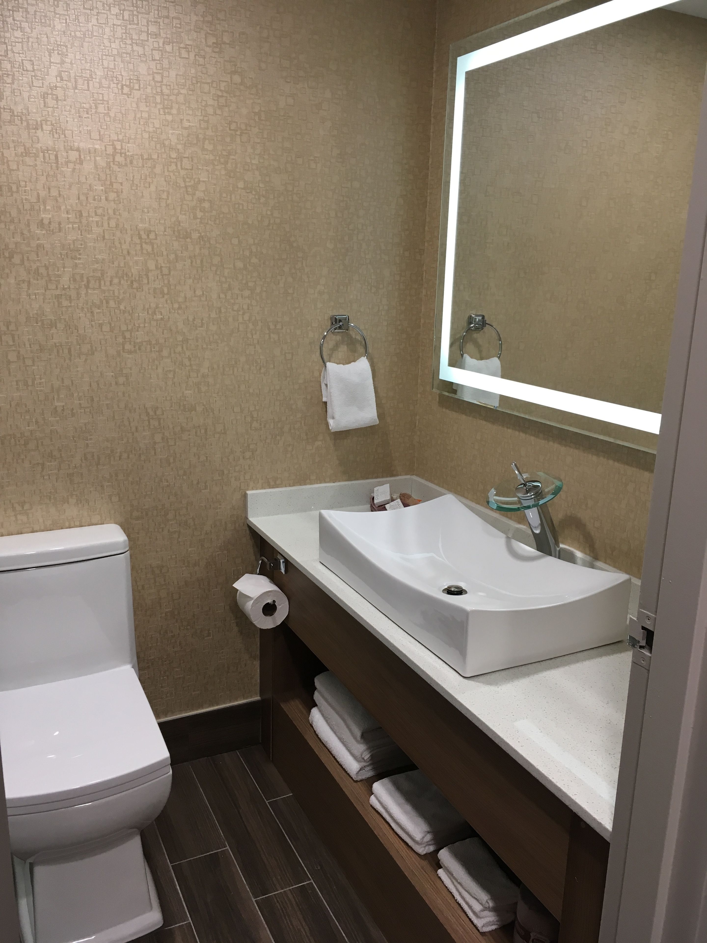 Une salle de bain moderne avec des toilettes blanches, un lavabo doté d’un receveur en verre et un miroir au-dessus du lavabo.