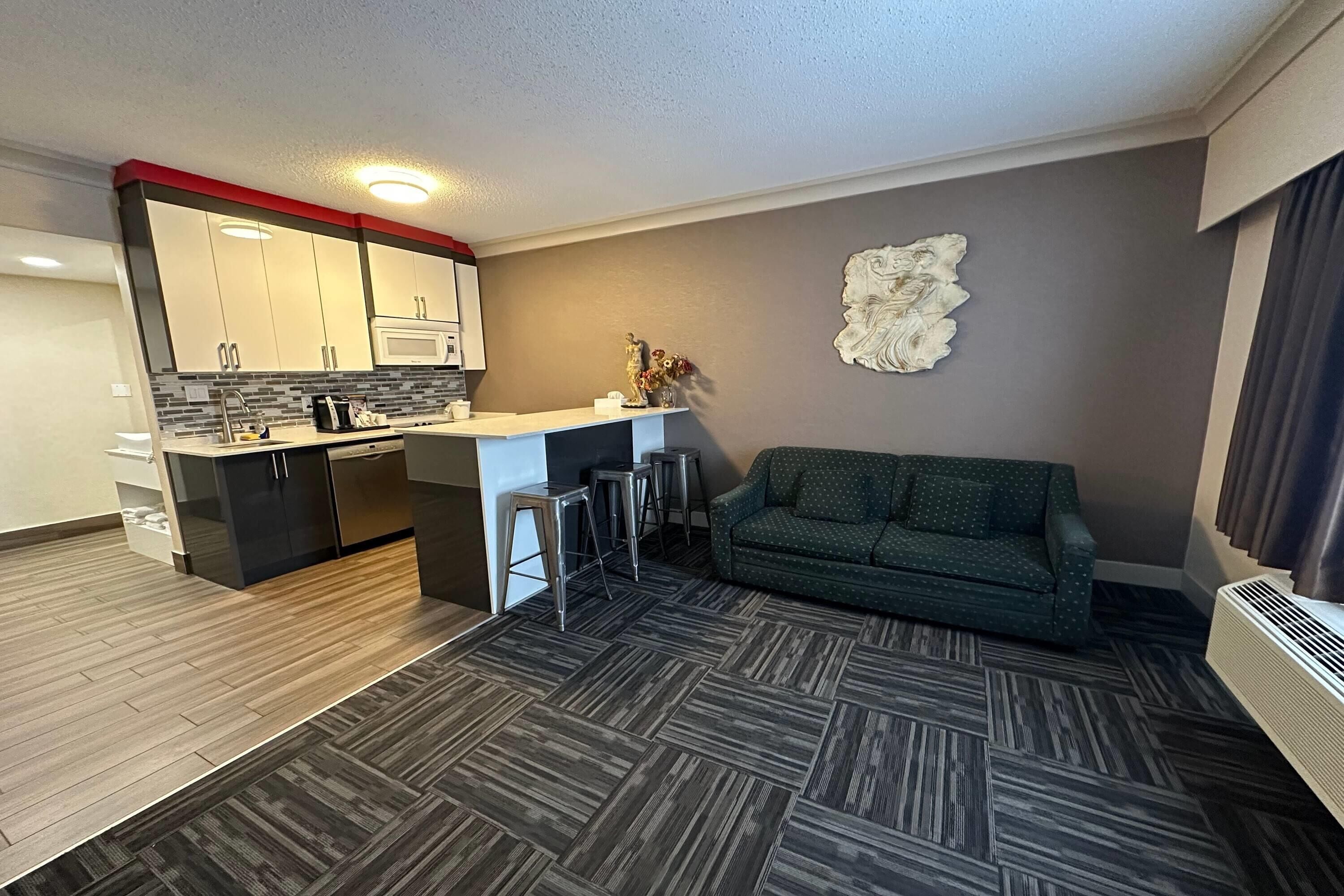 A modern kitchen with a microwave, a dining area with stools, a green sofa, and a decorative wall piece.