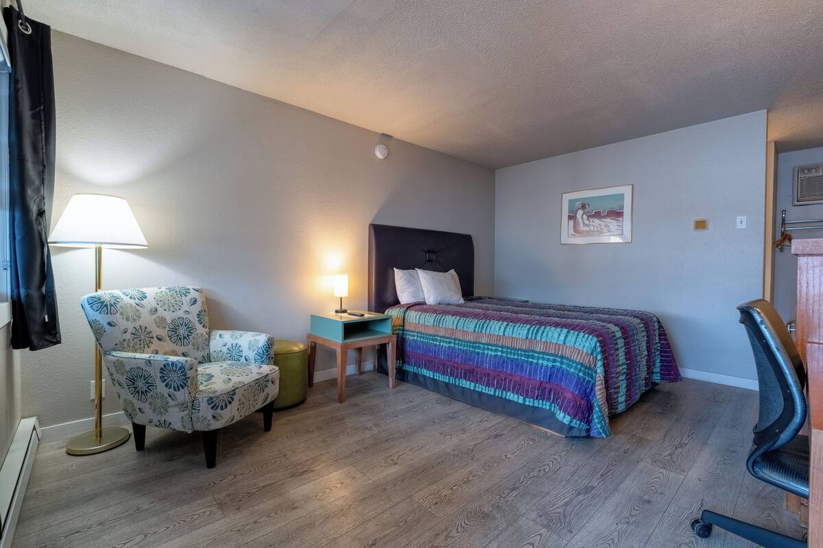 A bedroom with a bed, a chair, a nightstand, a lamp, and a picture on the wall.