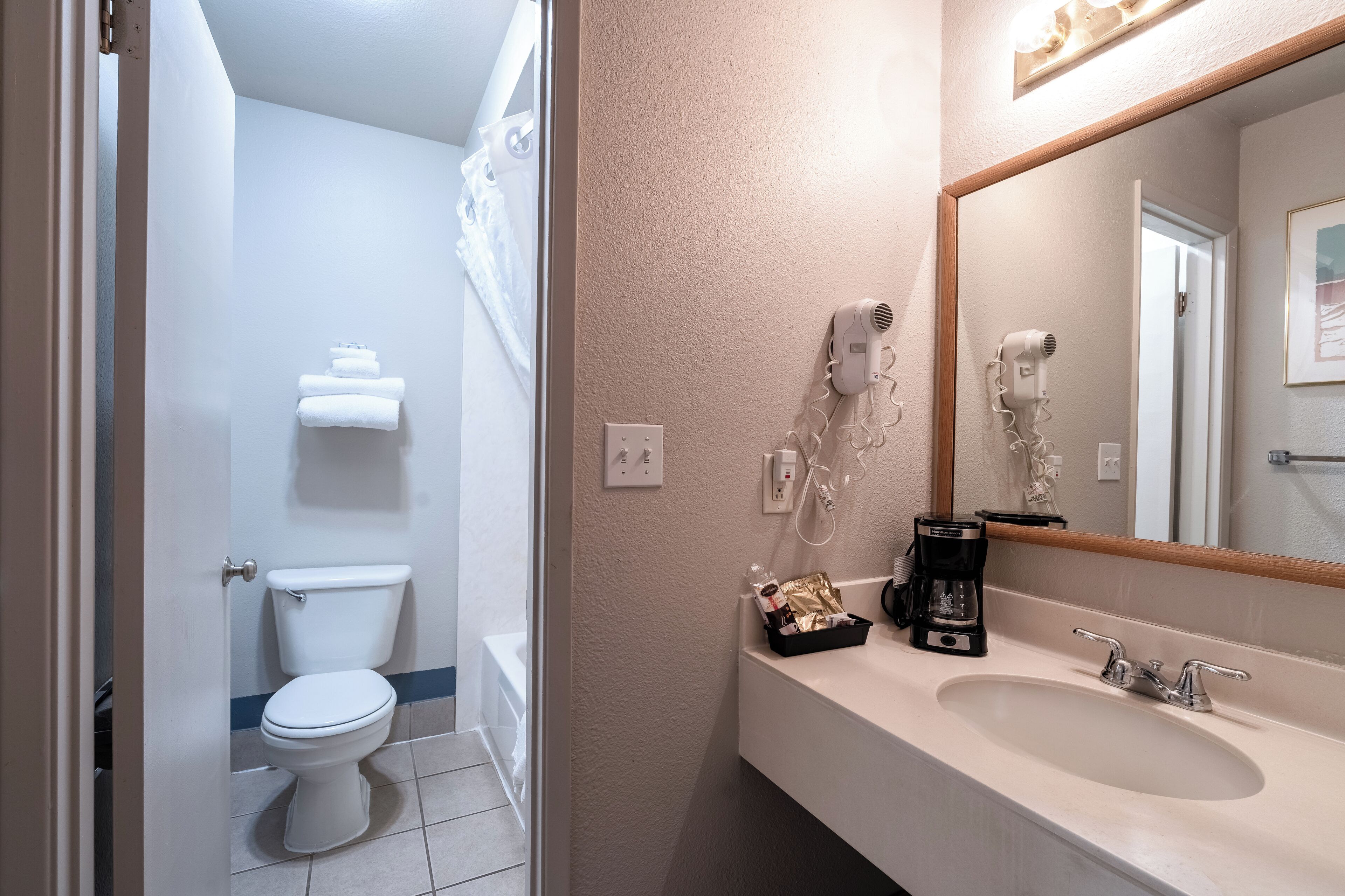 Une salle de bain équipée de toilettes, d’un lavabo, d’un miroir et d’un sèche-cheveux.