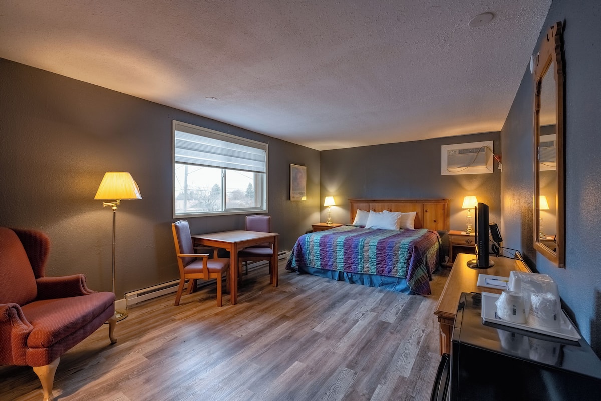 A hotel room with a bed, desk, chair, lamp, and a window.