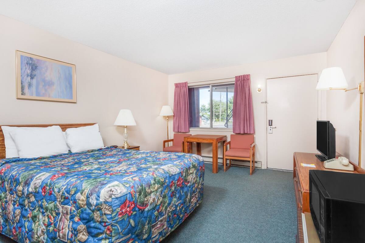 A hotel room with a large bed, a desk with a chair, a TV, and a window with curtains.