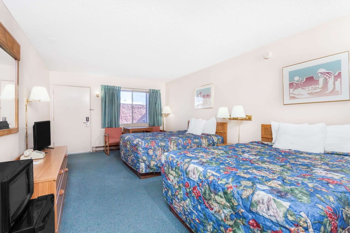 A hotel room with two beds, a desk with a computer, a TV, and a window with curtains.