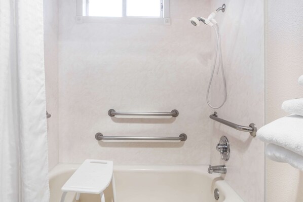 A bathroom with a bathtub, grab bars, a showerhead, and a window. - Days Inn by Wyndham Burns (Burns)