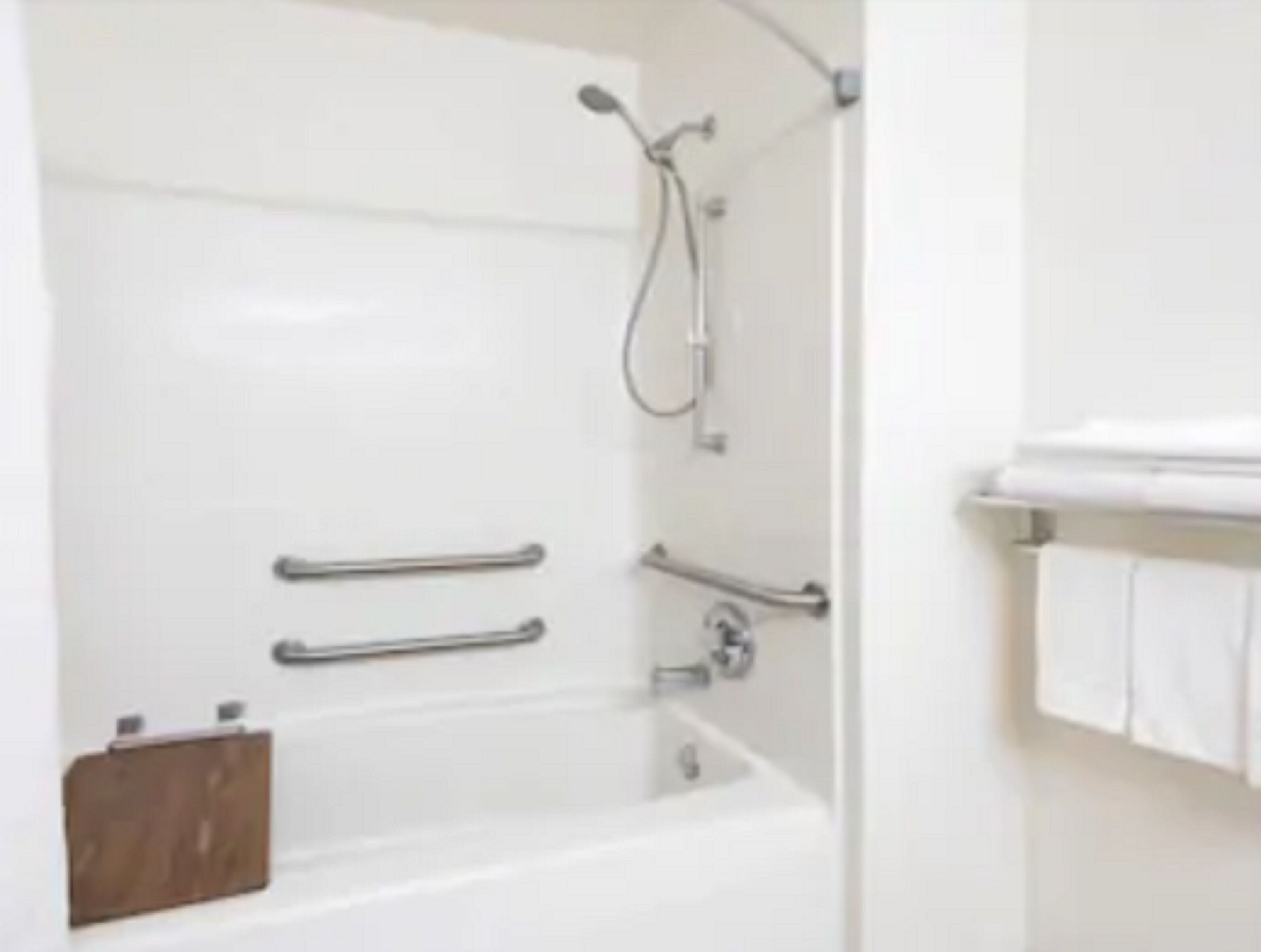 Ein modernes Badezimmer mit einer weißen Badewanne, Haltegriffen und einer Duschbrause.
