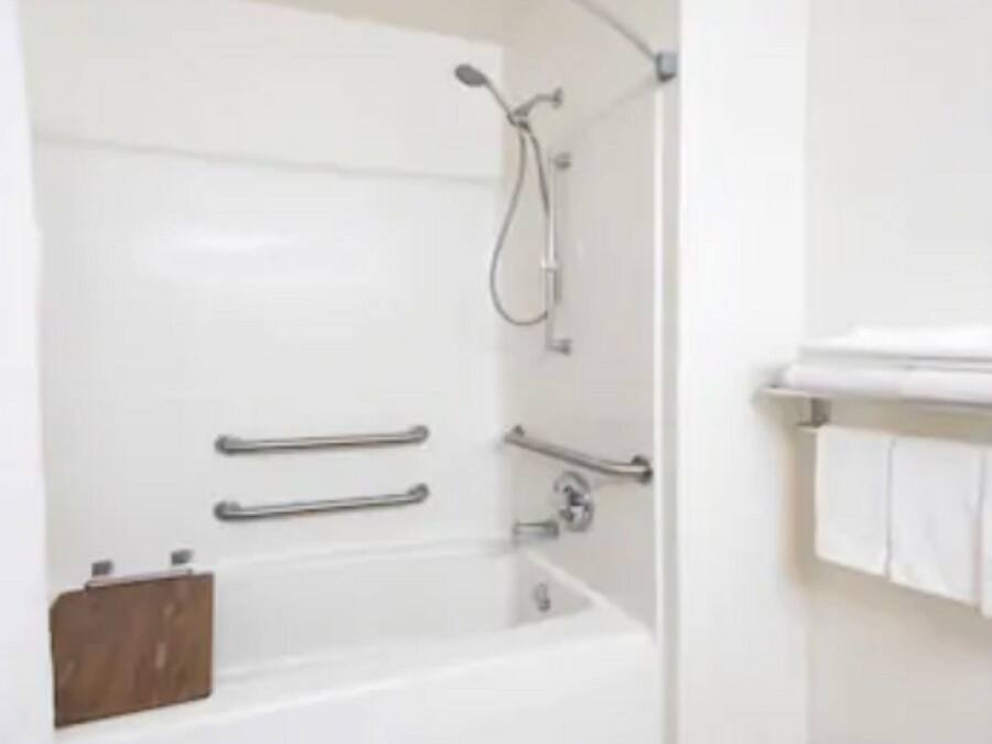 Ein modernes Badezimmer mit einer weißen Badewanne, Haltegriffen und einer Duschbrause.