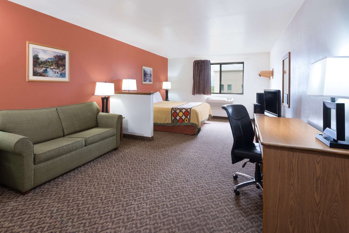 Habitación de hotel con un sofá verde, una cama con una colcha colorida, un escritorio con una computadora y dos lámparas.