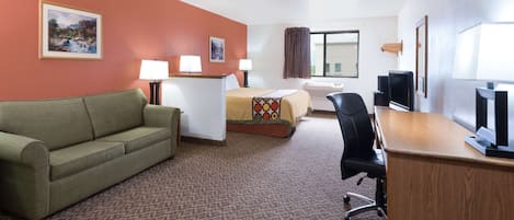 Hotelkamer met een groene bank, een bed met een kleurrijke deken, een bureau met een computer en twee lampen.