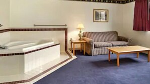 A hotel room with a bathtub, a sofa, a small table, and a lamp.