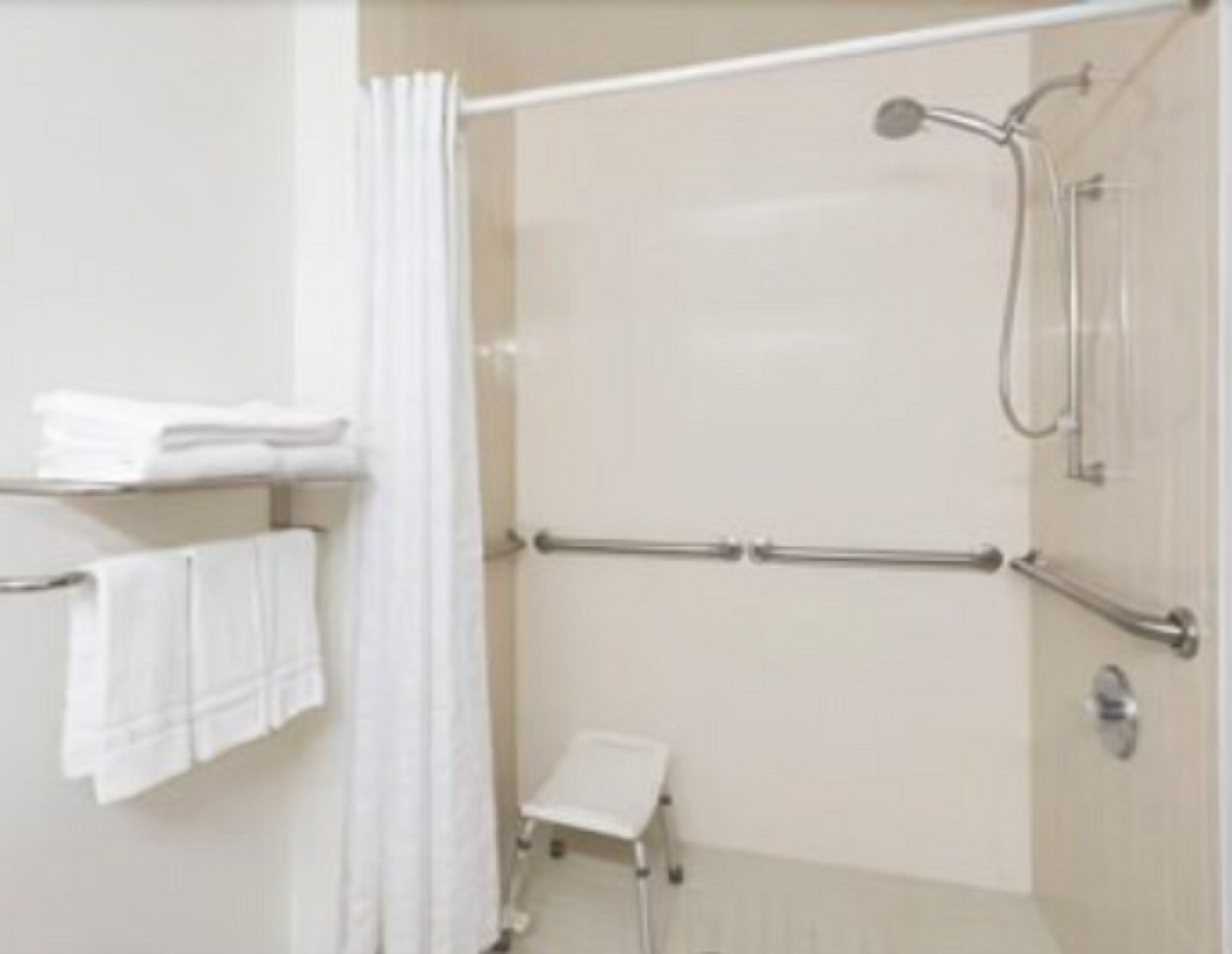 Un espacio de ducha con puerta de vidrio, un perchero blanco y un taburete pequeño de color blanco.