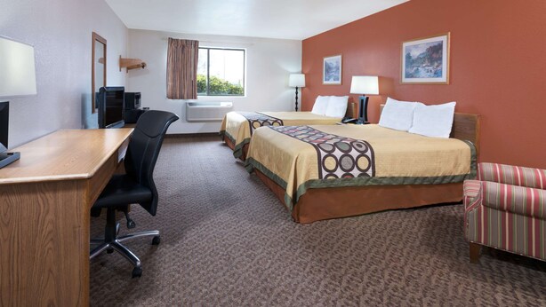 A hotel room with two beds, a desk, a chair, a television, and a window with curtains.