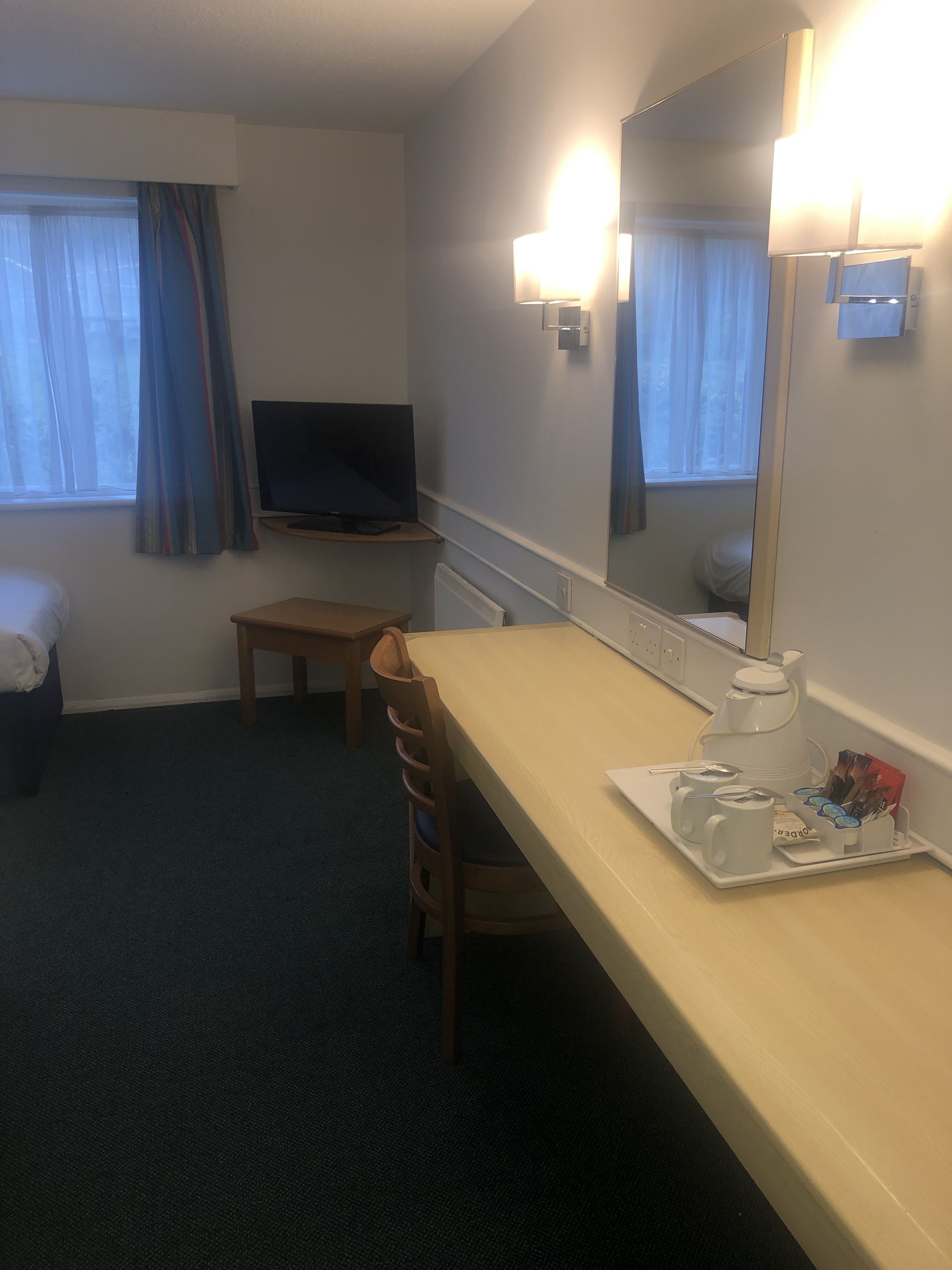 Habitación de hotel con una cama, un escritorio con silla, televisión y cafetera.